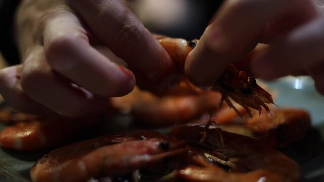Greasy hands take a fried shrimp tear off the head and clean it in a close up food scene showing texture juice and raw eating process of seafood cuisine