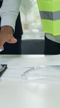Portrait of unrecognizable qualified multiracial specialists of building company in vests which demonstrating draft with construction to their experienced attentive manager in suit during meeting in