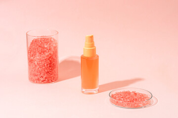 Soft pink cosmetic bottle with crystal salt on pastel background with shadows. Minimal skincare product, natural cosmetics concept
