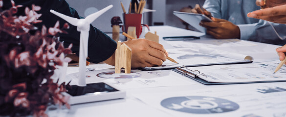 A modern office scene showcasing hands engaged in a sustainable project with a wind turbine model, eco-friendly documents, and collaborative efforts on green initiatives. SACTR