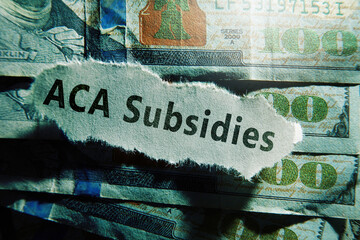 ACA Subsidies newspaper headline on hundred dollar bills -- Affordable Care Act aka Obamacare healthcare premium subsidy concept