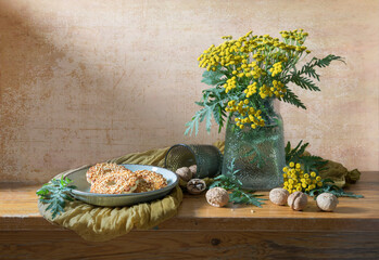 Still life in yellow and brown tones with a bouquet of yellow flowers, walnuts and confectionery