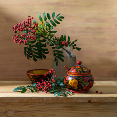 Still life with red rowan berries and wooden utensils painted with Khokhloma style