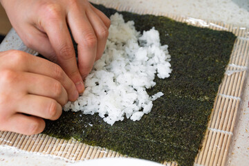Hands rolling sushi on bamboo mat with seaweed and rice