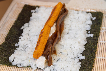 Homemade sushi roll preparation with rice, seaweed, and fish stick