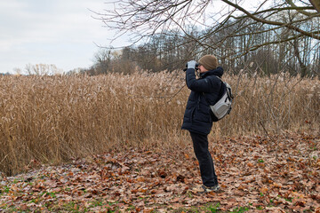 Caucasian male young adult birdwatcher in winter gear observing nature with binoculars