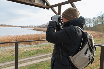 Caucasian male young adult birdwatcher in winter gear observing nature with binoculars