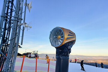 Snowmaking machine on ski slope with clear blue sky and people skiing