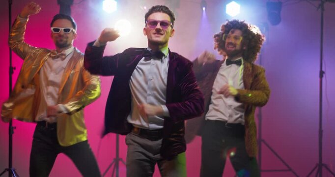 Dancers men trio party dance disco lights celebration. Lead performer fronts a synced routine while friends groove under vibrant lights on stage. Ideal for promotions. Retro fun party dance mood.