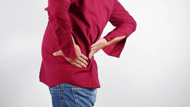 Lower back pain, young man experiencing lower back pain after working from home. An adult man holding and massaging his lower back, chronic back pain, bone calcification, osteoporosis. Healthcare conc