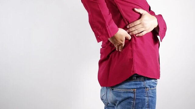 Lower back pain, young man experiencing lower back pain after working from home. An adult man holding and massaging his lower back, chronic back pain, bone calcification, osteoporosis. Healthcare conc