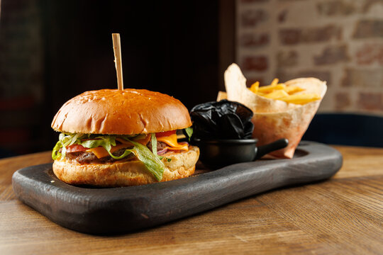 Enjoy a burger with fries served on a wooden board with a side of sauce in a cozy setting