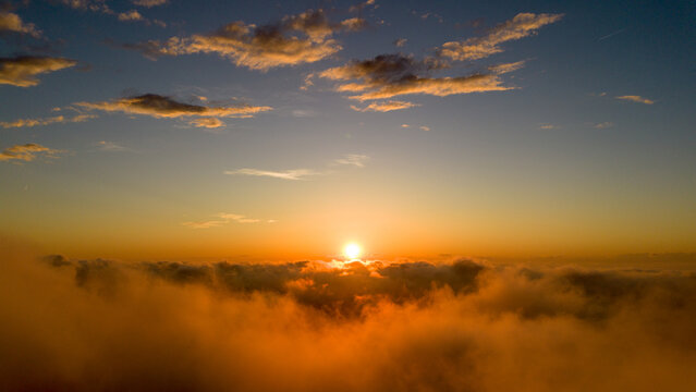 Overcast sunset sky with dramatic storm clouds above a suburban neighborhood and tree canopy, viewed from above with soft golden light on the horizon. - Powered by Adobe
