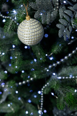 A textured white Christmas ornament hangs on a pine branch with soft blue bokeh lights in the background.