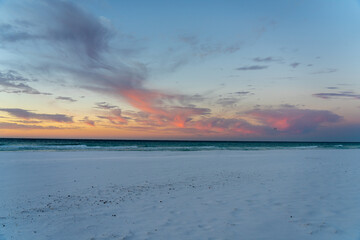 Obraz premium Pink clouds over a beach at sunset with kite surfer.