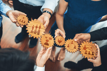 A group of diverse professionals collaboratively holding wooden gears with various icons, symbolizing teamwork, innovation, and strategic planning in a business environment. Amity