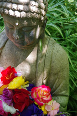 Weathered Buddha figure in a garden with colorful roses