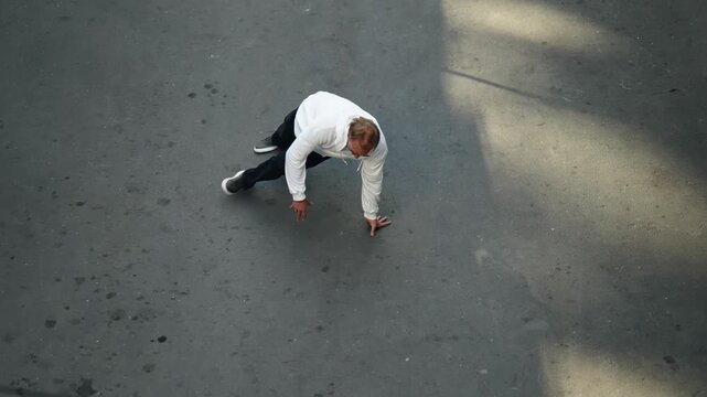 Overhead view of a street dancer in a white hoodie executing fluid floorwork on sunlit concrete, shown across two frames that emphasize movement, balance, and urban rhythm