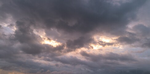 Fototapeta premium Dark storm clouds with soft sunlight breaking through at sunset, creating a moody dramatic sky background and weather concept with copy space.