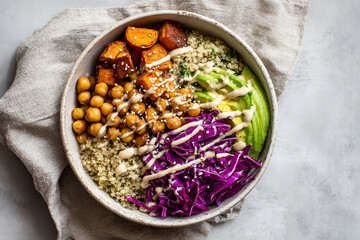 Fototapeta premium A vibrant bowl of quinoa topped with roasted sweet potatoes, chickpeas, red cabbage, avocado, and a drizzle of tahini. Ideal for healthy meal inspiration.