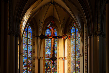 Interior of Gothic church central crucifix framed by vibrant stained glass, pointed arches, and ornate columns evoke reverence and spiritual grandeur.