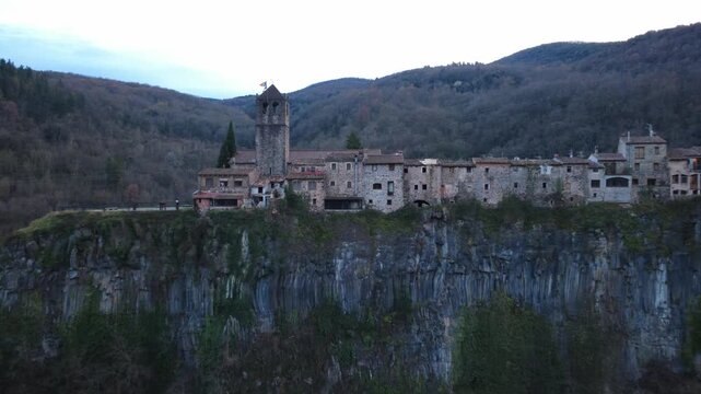 Aerial side view of Castellfollit de la Roca village built atop volcanic rock cliff.