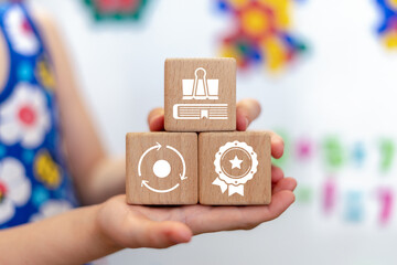 Young girl holding wooden blocks with icons symbolizing: modern education and school. Learning and education concept.