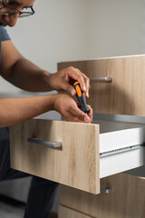 A carpenter carefully adjusts the screws of a drawer handle indoors, ensuring proper fit and durability in furniture construction.