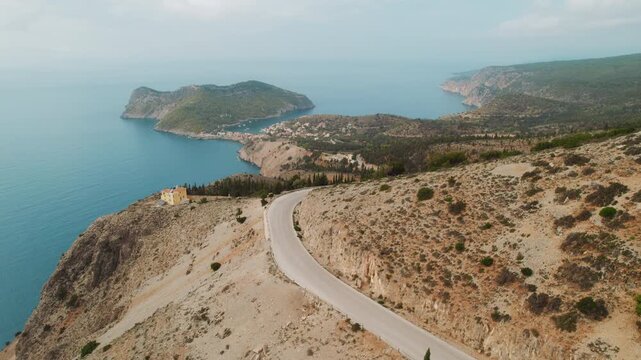 Car moving on coastal road above a tranquil Ionian bay and hillside Asos village on a clear summer day in Kefalonia