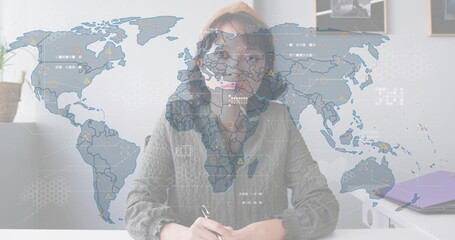 Writing Asian woman wearing beanie and glasses at home office desk, holding pen, data overlay