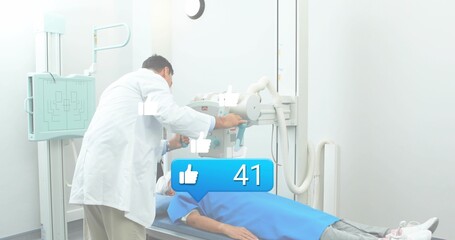 Adjusting tech in labcoat leaning over patient in blue gown, aiming xray tube above chest, bubble41