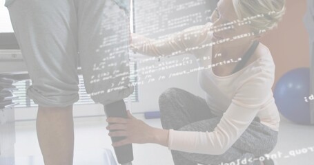 Adjusting kneeling therapist fitting prosthetic leg on patient in clinic, wearing gray leggings