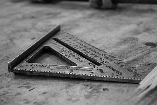 Metal carpenter square measuring tool on workbench in black and white
