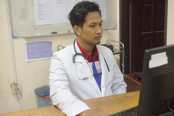 Focused young medical practitioner man working at computer in doctor office, typing on keyboard, writing electronic medical records, examination reports, using modern technology