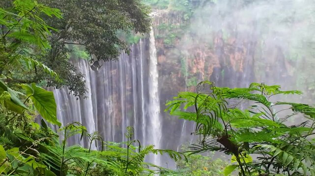 The multi-tiered Tumpak Sewu waterfall, with its lush greenery and wide stream of water flowing into a deep, semi-circular basin on the island of Java. Near Mount Semeru. Indonesia. 4К