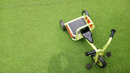 Top view of a small children’s tricycle lying on its side on bright green grass, with empty seat...