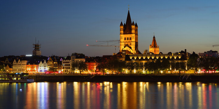 Atmospheric night shot of the illuminated Great St. Martin church and Cologne&rsquo;s old town with colorful light reflections on the Rhine river