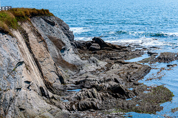CliffRocky coastal shoreline with layered stone cliffs and ocean waves at low tide. Natural seascape showing erosion, textures, and rugged coastal geology under clear daylight.
