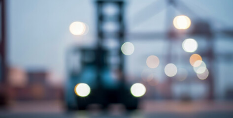Forklift illuminated by city lights operates in an industrial area. Blurred background emphasizes the machinery's role in the urban environment and logistics.
