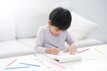 Naklejka premium 白いリビングで色鉛筆を使い、夢中でお絵かきやぬり絵を楽しむ幼児 想像力や創作力を育む、非認知能力を育てる