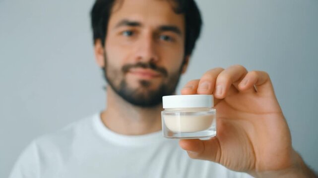 Bearded man presenting a small jar of organic skincare products