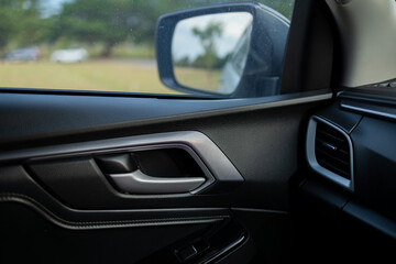 Modern Car Interior Door Handle and Side Mirror View,Close-up of a stylish interior door panel of a modern vehicle, featuring a matte silver door handle, textured black trim, 