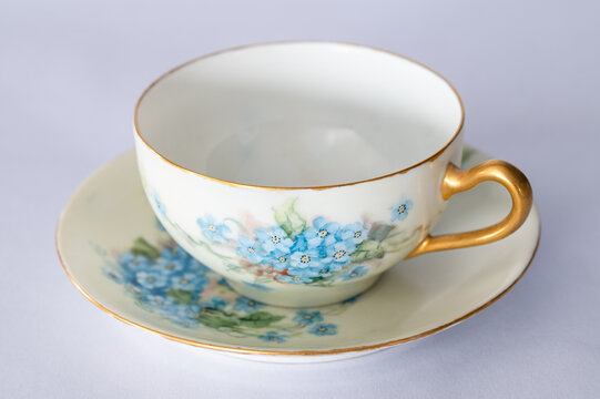 Empty teacup on a saucer, painted with blue Forget-Me-Not flowers, white background