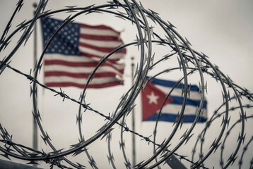 Sharp razor wire coils in front of blurred USA and cuban flags symbolizing political tension