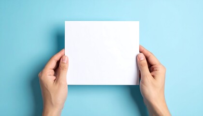 Fototapeta premium Hands holding a blank white card against a blue background.