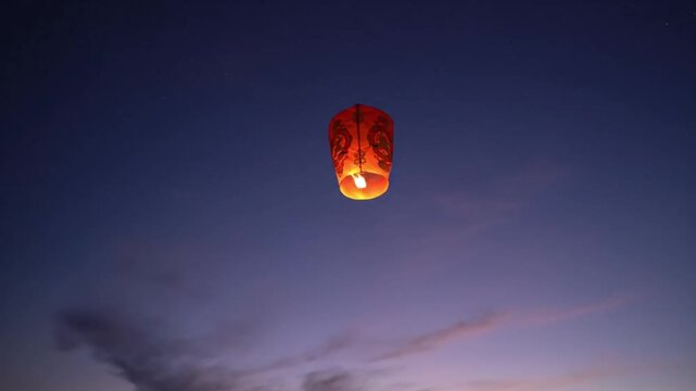 A glowing lantern flies through a serene sunset sky with mountains in the background, symbolizing freedom and adventure