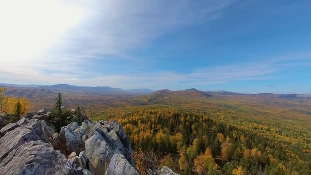 A scenic view from the top of the rocks, overlooking the vast, endless taiga and mountain ridges of the Southern Urals during the golden autumn season. The remote, wild nature landscape in Bashkortost