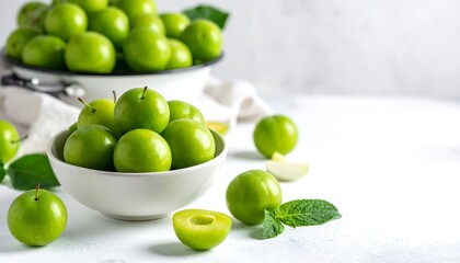 Bowl and pot filled with plump, vibrant green plums. Light, bright and clean, with mint leaf garnish