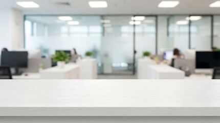 A blurred view of an open plan office space with multiple workstations a white desk foreground and people working in the background