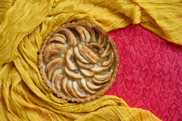 Happy Valentine’s Day, thinly sliced apples elegantly arranged in a French Apple Tart, Tarte Aux Pommes, on a red background with heart shapes and gold glitter and gold fabric
